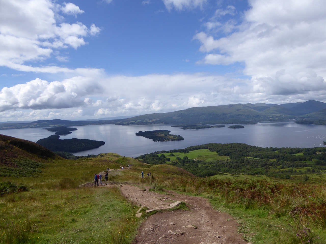 Walkers descending the Conic Hill path toward Loch Lomond and its islands—faces not identifiable at this distance.
