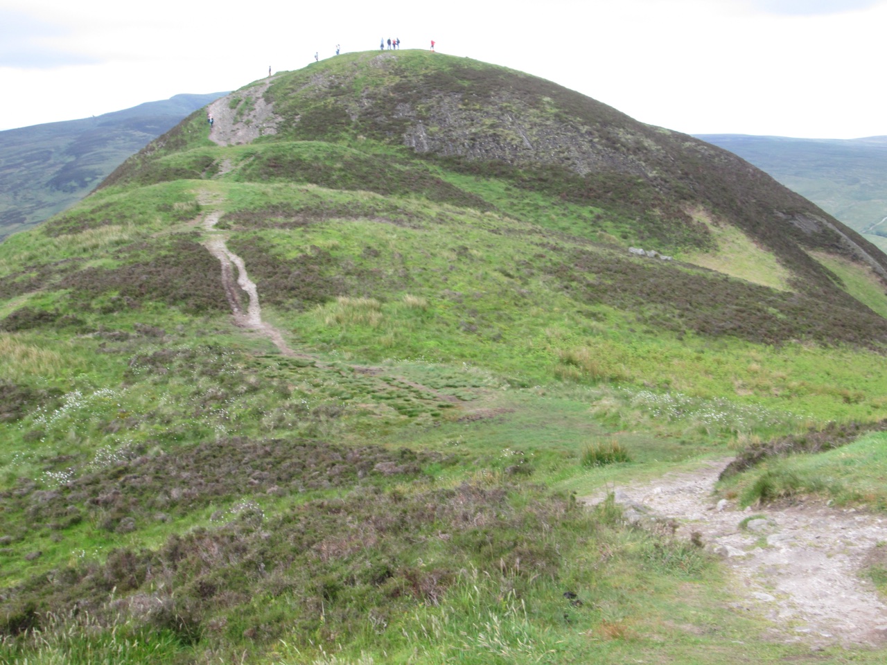 Walkers on the summit of Conic Hill, with the ascending hillside path below.