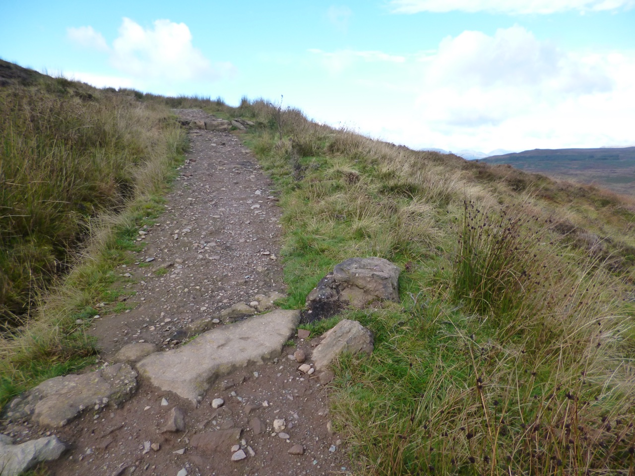 Rocky path climbing Conic Hill on the West Highland Way under a bright sky.